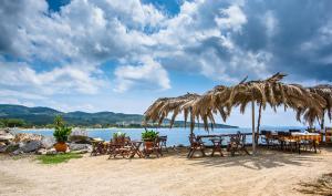 a group of tables and chairs under a straw umbrella on a beach at Greek House Hotel in Neos Marmaras