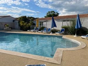 a swimming pool with chairs and blue umbrellas at Le Petit Bois in Sainte-Marie-de-Ré