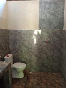 a bathroom with a toilet and a tiled wall at Tropicana Gili in Gili Meno