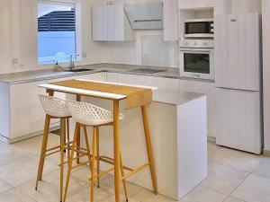 a kitchen with white cabinets and a table and stools at Villa - Cosy - Piscine - Guadeloupe centre in Baie-Mahault