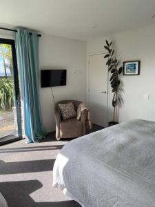 a bedroom with a bed and a chair and a television at Raglan Studio at The Coastal Retreat in Raglan