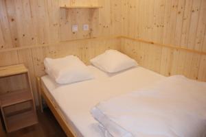 a bedroom with two white beds and a wooden wall at Roulottes cocooning au coeur des Landes in Mées