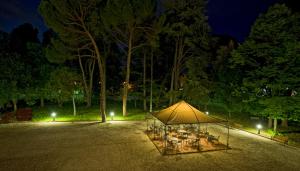 Villa Raffaello Park Hotel في أسيسي: خيمة مع طاولات وكراسي في حديقة في الليل