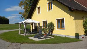 a yellow house with a table and an umbrella at Ferienwohnung Waldhäusl in Oberrosenauerwald