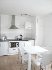 a white kitchen with a white table and white chairs at Les Mini-lofts de Paul et Virginie in Wimereux