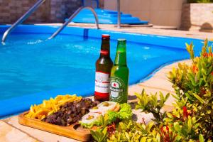 two bottles of beer and a plate of food next to a swimming pool at FLAT BADEJO in Japaratinga