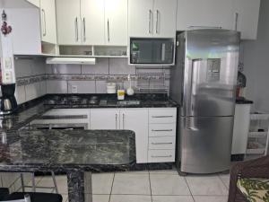 a kitchen with white cabinets and a stainless steel refrigerator at Apartamento no Costão do Pântano do Sul in Florianópolis