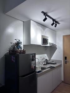 a kitchen with a black refrigerator and white cabinets at Cozy Near Mall SM Fairview Trees Residences Quezon City in Manila