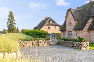una casa antigua con una pared de piedra y un camino de entrada en Reetdachhaus Reetkoje Reetdachhaus Reetkoje I, en Süderhöft