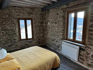 a bedroom with stone walls and a bed and two windows at Chalet confortable à Ascou avec vue sur la montagne in Ascou
