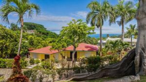 リンコンにあるCasita 4 at Ceiba Tree Inn. Tranquility with Garden Views and Pergola with Ocean Overlookの赤い屋根とヤシの木がある黄色い家