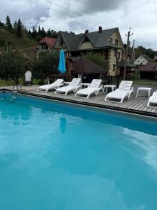 a swimming pool with white chairs and an umbrella at Живописні карпати in Slavske