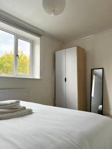 ein Schlafzimmer mit einem weißen Bett mit einem Schrank und einem Fenster in der Unterkunft Beautiful 2-Bed City Centre Apartment with Balcony in Milton Keynes