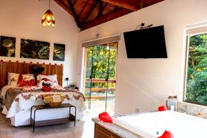 a bedroom with a bed and a tub and a tv at Chalé Canto do Galo 2 - Hidro da Jacuzzi, Lareira Ecológica, Cozinha Completa, Wi-Fi 80mbps, próximo a comércio local e relaxando ao som do riacho in Gonçalves
