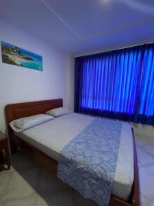 a bedroom with a bed and a window with blue curtains at Alojamiento Peñón del rodadero in Santa Marta