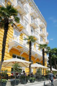 un bâtiment jaune avec des palmiers, des tables et des parasols dans l'établissement BRISTOL Hotel Opatija, à Opatija