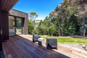 a wooden deck with two chairs on a house at Wavesong Whakaaio 11D, 100 metres to Onetangi Beach - Be My Guest in Onetangi