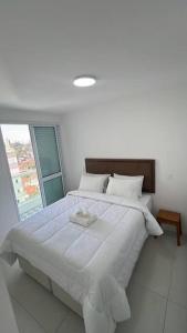 a white bedroom with a large bed with a window at SJC Funcional e Aconchegante in São José dos Campos