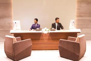 Dois homens de fato sentados numa secretária com computadores portáteis. em Space Hotel and Apartments em Daca
