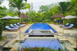 a pool with chairs and umbrellas next to a resort at Fullara 1 BR Suite With Rice Field View ZN240 in Ubud