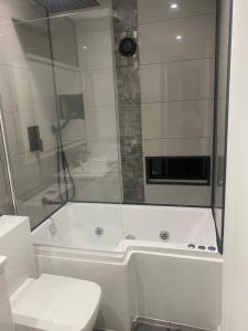 a white bathroom with a shower and a toilet at Lovely Modern studio flat with jacuzzi bath free parking in Stanwell