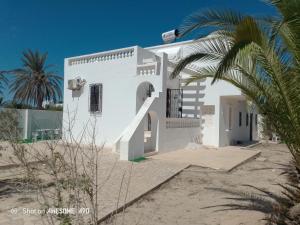 a white house on the beach with a palm tree at Maison La rose 1 in Mezraya