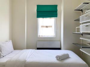 a bedroom with a white bed with a green curtain at Modern Look and Comfortable 2BR Green Pramuka City Apartment By Travelio in Jakarta