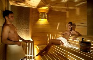 Un uomo e una donna seduti in una sauna di Hotel Ladinia Dolomites View a Pozza di Fassa