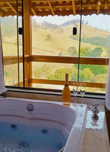 a bath tub with two wine glasses and a window at Chalés Recanto na Serra in Gonçalves