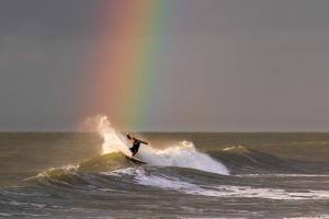 a man riding a wave on a surfboard in the ocean at Bambou Rooms in Vrouwenpolder +5 photos