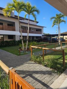 a fence with palm trees in front of a building at Village Térreo Acqua Guarajuba in Guarajuba