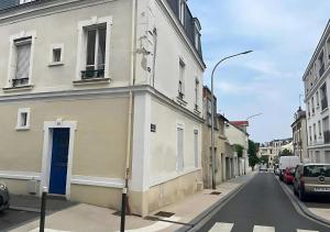 Una calle vacía con un edificio blanco con una puerta azul. en Cozy APT in Le Perreux with Parisian Charm & Disneyland Fun, en Le Perreux-Sur-Marne