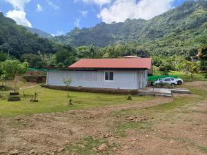 a white house with a red roof in a field at Pitake Lodge 1 in Nuku Hiva