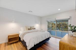 Un dormitorio blanco con una cama y una ventana grande. en Lakeside Retreat, en Long Jetty