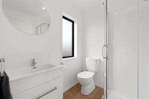 a white bathroom with a toilet and a mirror at Frankton Townhouse Retreat - Central in Hamilton