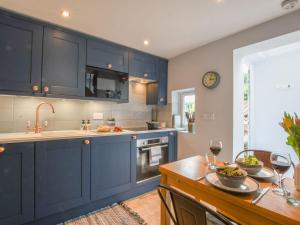 eine Küche mit blauen Schränken und einem Tisch mit Weingläsern in der Unterkunft Caines Cottage in Saxmundham