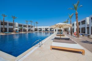 a large swimming pool with a umbrella and palm trees at Reef Oasis Beach Aqua Park Resort in Sharm El Sheikh