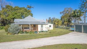 une maison blanche avec un toit gris et une allée dans l'établissement Cane Cutters Cottage, à Woombah