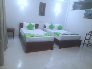 two beds with green pillows in a room at Wildescape Polonnaruwa in Polonnaruwa