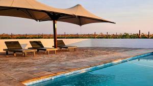 zwei Stühle und ein Sonnenschirm neben einem Schwimmbecken in der Unterkunft Kitchen51 Cottages in Keetmanshoop