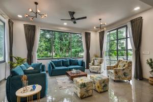 sala de estar con muebles azules y ventanas grandes. en SaffronStays Magnolia - 3BHK Moira Goa Villa with Pool & Games Room, en Bardez