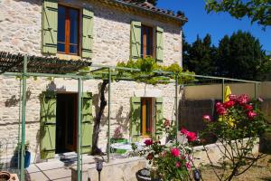 a stone house with green shutters and flowers at Sous La Treille in Saze
