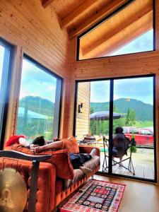 two people laying on a couch in a room with large windows at Cazare Cabana Pensiuni Vatra Dornei Bucovina cu Ciubar in Iacobeni +69 photos