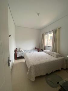 une chambre blanche avec deux lits et une fenêtre dans l'établissement Morada da praia, à Bertioga