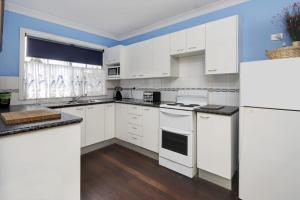 a white kitchen with white appliances and blue walls at Sunseekers at Hat Head - 44 Bay Street in Hat Head +8 photos