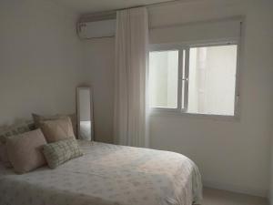 ein weißes Schlafzimmer mit einem Bett und einem Fenster in der Unterkunft Casa de Verão no Condomínio Porto Coronado in Xangri-lá