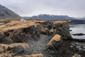a small white house on the shore of a body of water at Grund in Rauðamelur