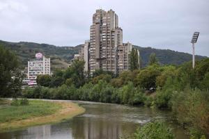 a river with tall buildings in the background with buildings at Apartman Lamela in Zenica