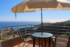 a table and chairs on a balcony with an umbrella at The View House in Ponta do Sol