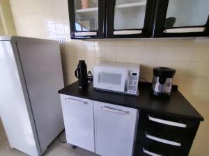a kitchen with a counter with a microwave and a refrigerator at Apartamento no centro, com garagem e wi-fi in Peruíbe